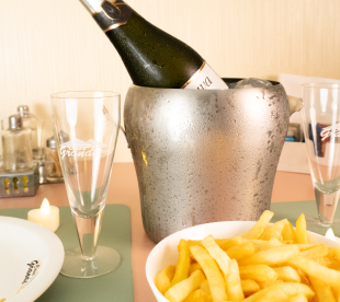 Garrafa de espumante em balde de gelo com taças ao lado e porção de batatas fritas em primeiro plano.